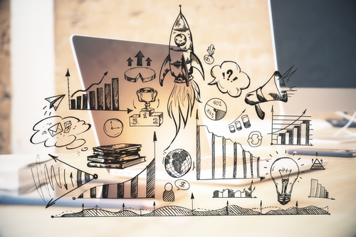 Desk with sketches of growth: rocket launch, bar charts, trophy, lightbulb, megaphone, and arrows around a laptop.